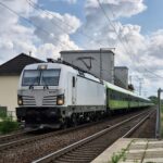 White and green train traveling through Deutschland on a cloudy day.